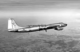 Photographie en noir et blanc d'un avion en vol, avec, en fond, la surface de la Terre.