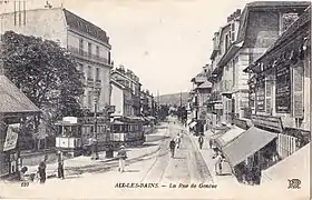 Carte postale en noir et blanc représentant une rue parcourue par des tramways.