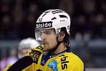 Photographie d’un hockeyeur, de buste, de trois-quarts, maillot jaune et casque blanc, regardant devant lui