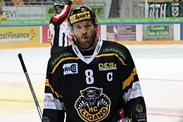 Photographie couleur d’un hockeyeur, de face, en buste, la tête légèrement penchée sur sa droite.