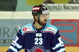Photo couleur d’un hockeyeur, de buste, portant une barbe de quelques jours, la tête tournée vers sa gauche