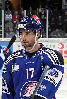 Hockeyeur, de buste, de trois quart face, portant maillot et casque bleu, le regard fuyant sur sa droite