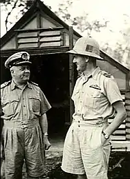 Deux hommes en uniformes militaires de couleur pâle, l'un d'entre eux porte un casque de combat.