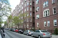 Vue d'une rue avec plusieurs voitures garées le long de façades d'immeubles identiques.