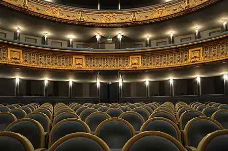 Salle éclairée : les fauteuils du parterre et la balcons aux décors dorés.