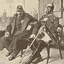 Les deux hommes sont assis côte à côte. Les deux sont en uniformes, Bismarck a un casque à pointe, Napoléon un képi. Alors que Bismarck se tient droit avec le menton haut, Napoléon est avachi sur sa chaise.