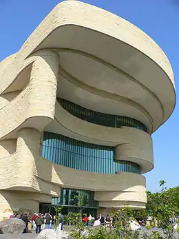 Vue extérieure d'un musée amérindien, constitué de deux niveaux en plus du sol, un toit surplombant largement l'entrée.