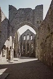Photographie d'une nef ruinée d'église, dont restent les murs, une ogive et le chevet.