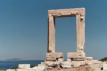 photographie : un portique de marbre se dressant seul au bord de la mer