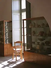 photographie : des objets archéologiques dans des armoires encadrant une fenêtre par où entre le soleil