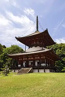 Une grande tour à un étage en forme de pagode avec une base carrée et un étage supérieur rond. Les murs sont blancs et les poutres rouge fané.