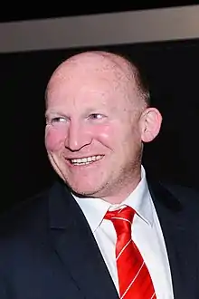 Photograhpie d'un homme portant un chemise blanche, une cravate rouge et une veste de costume noire