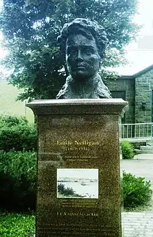Tête en bronze d'un homme avec une chevelure abondante, sur socle en marbre, placé dans un parc.