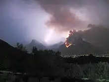 Montagne en feu dans la nuit, avec un éclair qui s'abat en arrière-plan.