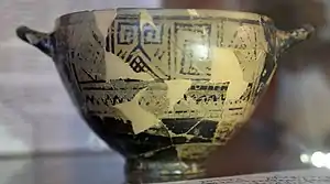 « Coupe de Nestor », du côté de l'inscription, v. 720 av. J.-C., musée archéologique de Pithécusses (haut) et transcription de l'inscription avec la reconstitution des passages perdus (bas). Traduction : « Agréable est de boire dans la coupe de Nestor, mais quiconque boit de cette coupe est aussitôt saisi du désir d'Aphrodite à la belle couronne. »