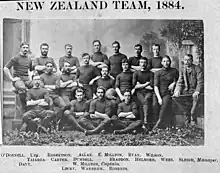 Photographie en noir et blanc. Portrait officiel d'un groupe d'hommes habillés en tenue de sport noire, alignés sur trois rangs, assis ou debout.