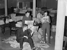 Trois hommes en habits cravates examinant des revues et des journaux dans un bureau.