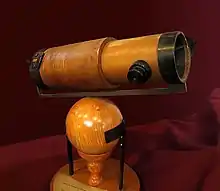 Un télescope en bois est monté sur une sphère et un socle de même.