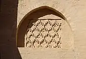 Photographie d'une niche en arc brisé, à fond plat. Ce dernier est orné d'un décor géométrique losangé en briques cuites. L'arc est le vestige d'une ancienne porte murée de la façade occidentale.