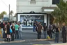 Image de personne devant une affiche promotionnelle pour un concert de Nightwish