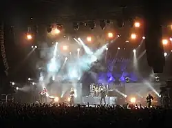 image d'un groupe de rock, composé de cinq membres, jouant devant grand public