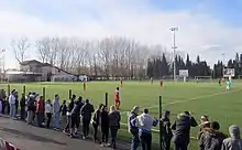 Photographie en couleur prise en tribune d'un terrain avec deux équipes au coup d'envoi d'un match de football.