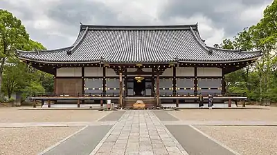 Hall doré du temple bouddhiste Shingon Ninna-ji, vue de face. Fondé en 888 par l'empereur Uda, Ninna-ji fait partie des monuments historiques de l'ancienne Kyōto inscrits au patrimoine mondial de l'UNESCO depuis 1994. Photo prise durant une cérémonie. De nombreuses paires de chaussures patientent au pied de l'escalier. Juin 2019.