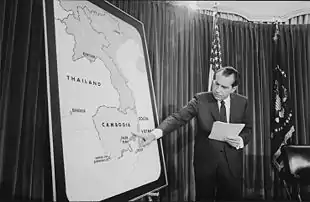 Richard Nixon, à droite de cette photo en noir et blanc, tient un papier dans sa main gauche et de la droite pointe la région de la province de Svay Rieng sur une carte de la péninsule indochinoise.