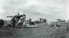 Photo noir et blanc de trois canons en batterie, sur des affûts surélevés, les servants s'affairant.