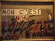 Collage féministe de feuilles au format A4 reprenant avec un caractère par page le slogan « Non c'est non », en lettres noires et rouges. Le slogan recouvre partiellement d'autres revendications en écriture cursive, faisant notamment état de viol et d'assassins.