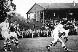 Photo noir et blanc de joueurs de football Tchècoslovaques en maillots blanc défendant devant un attaquant irlandais en maillot vert qui frappe le ballon de la tête en direction du but.