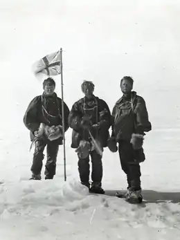 Trois hommes se tenant près d'un drapeau.
