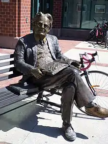 Picture of the Northrop Frye bronze statue. He is sat on a bench with a book in his lap.