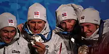 Photo de quatre hommes de face, chacun montrant leur médaille