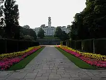 Un bâtiment blanc surmonté d'une tour, au bout d'une allée fleurie.