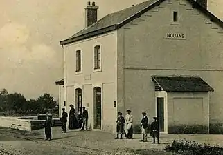 Photographie en noir et blanc d'une station ferroviaire et de voyageurs attendant un train.