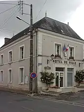 Photographie en couleurs d'un bâtiment portant l'inscription « HOTEL DE VILLE» en façade et décoré de drapeaux.