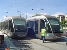 Image représentant les essais sur le boulevard Jean-Jaurès avec deux tramways à l'arrêt et un homme en gilet jaune traversant la voie du tramway.