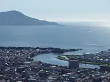 Photo couleur montrant l'embouchure d'un fleuve se jetant dans la mer, sous un ciel bleu.