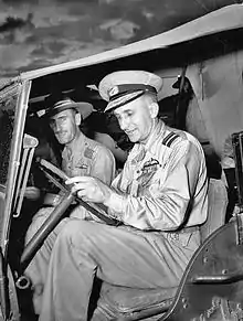 Deux hommes en uniformes militaires clairs assis dans une jeep.