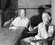 Deux hommes en uniforme clair assis à une table.