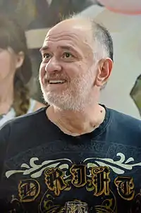 Photo en couleurs d'un homme légèrement barbu, en tee-shirt bleu, souriant et regardant vers le haut.