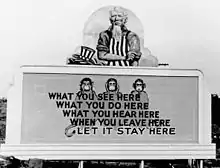 Oncle Sam a posé son chapeau et remonte ses manches. Sur le panneau situé en dessous de lui se trouvent les trois singes de la sagesse et le slogan : What you see here / What you do here / What you hear here / When you leave here / Let it stay here.