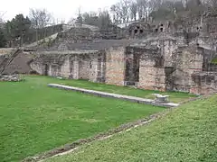 Vestige du portique avec son stylobate et une base de colonne. Le dallage du portique est couvert d’un gazon de protection.