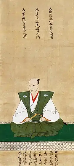 Oda Nobunaga vêtu de vert et de blanc, assis en tailleur, et inscriptions en caractères chinois.