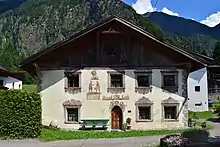 Bâtiment aux murs blancs et au toit en bois noir de style suisse avec montagnes en arrière-plan en été.