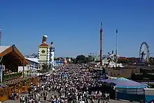 Oktoberfest 2007, grande foule entre tentes et attractions foraines avec en second plan la tour surmontée d'une chope de bière Paulaner