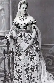Photographie noir et blanc montrant une femme en grande robe à motifs fleuris.