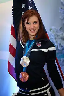 Une femme rousse portant deux médailles olympiques, debout devant un drapeau américain.