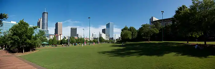 Un parc avec de vastes espaces d'herbes et quelques arbres devant plusieurs gratte-ciel.